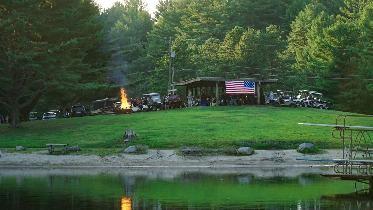 A campfire on the lawn above the lake with campers beyond